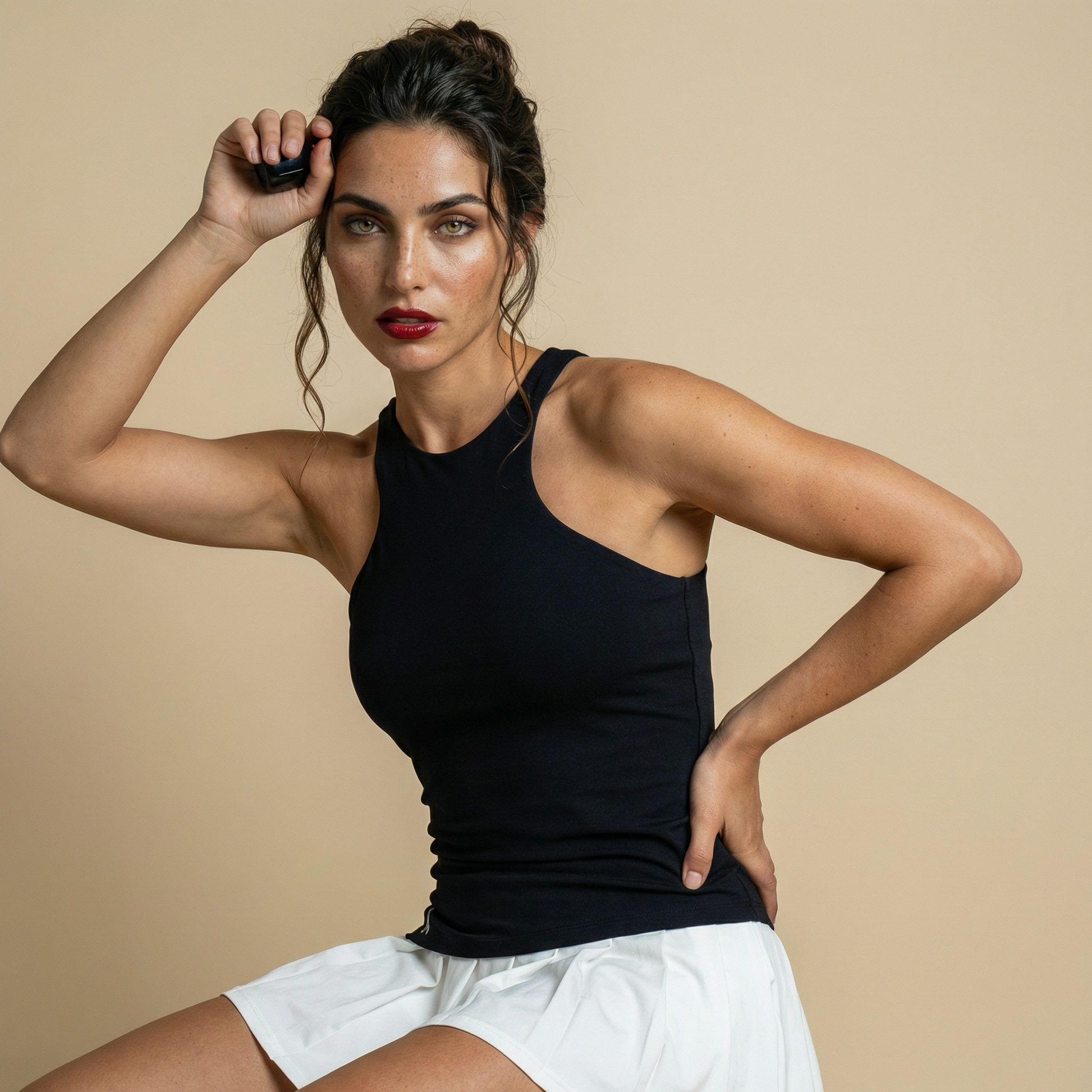 Woman wearing a black asymmetric athletic tennis dress with white pleated skirt detail, posing in studio against a beige background.