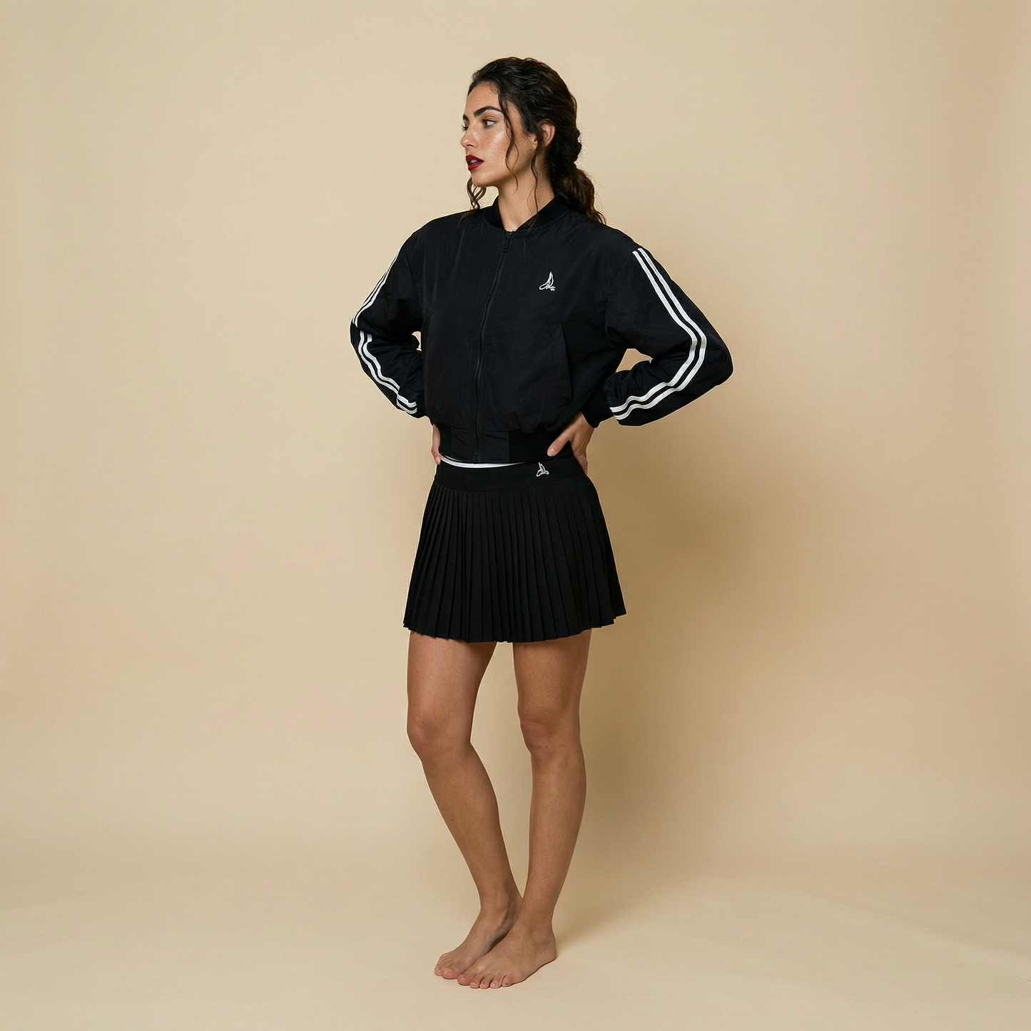 Women’s black padded padel and tennis bomber jacket with stripe sleeves styled with pleated skirt – Noir Court Bomber UK