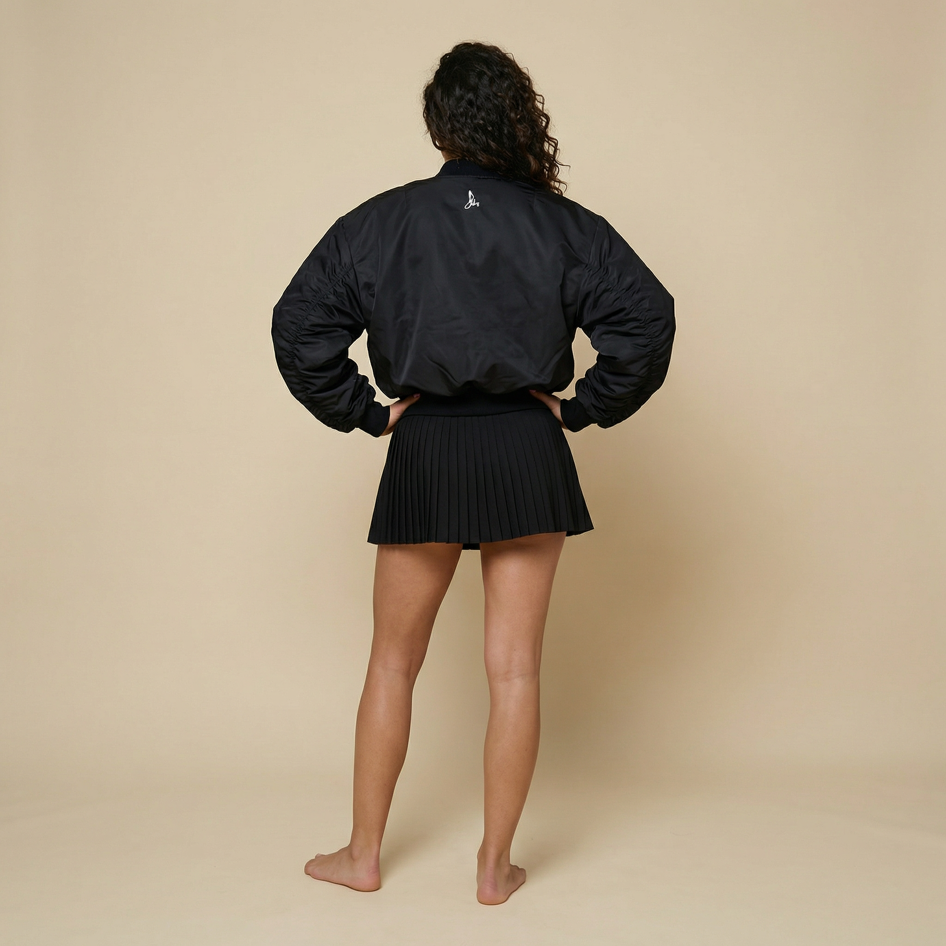 Full back view of women’s black padded padel and tennis jacket with ribbed hem – Noir Court Bomber UK